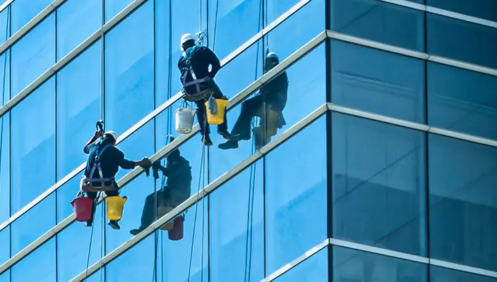 Técnico de Aires Limpieza realizando limpieza de cristales en altura en un edificio corporativo de Santiago.